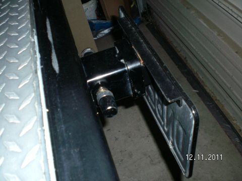 1996 Ford Bronco - Low-angle shot of a black receiver-hitch mounted license plate bracket bolted into the square receiver tube, with a pin and clip through th…