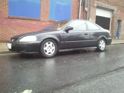 1999 Honda Civic - A dark 1999 Honda Civic coupe is parked on a wet street in front of a brick building.
