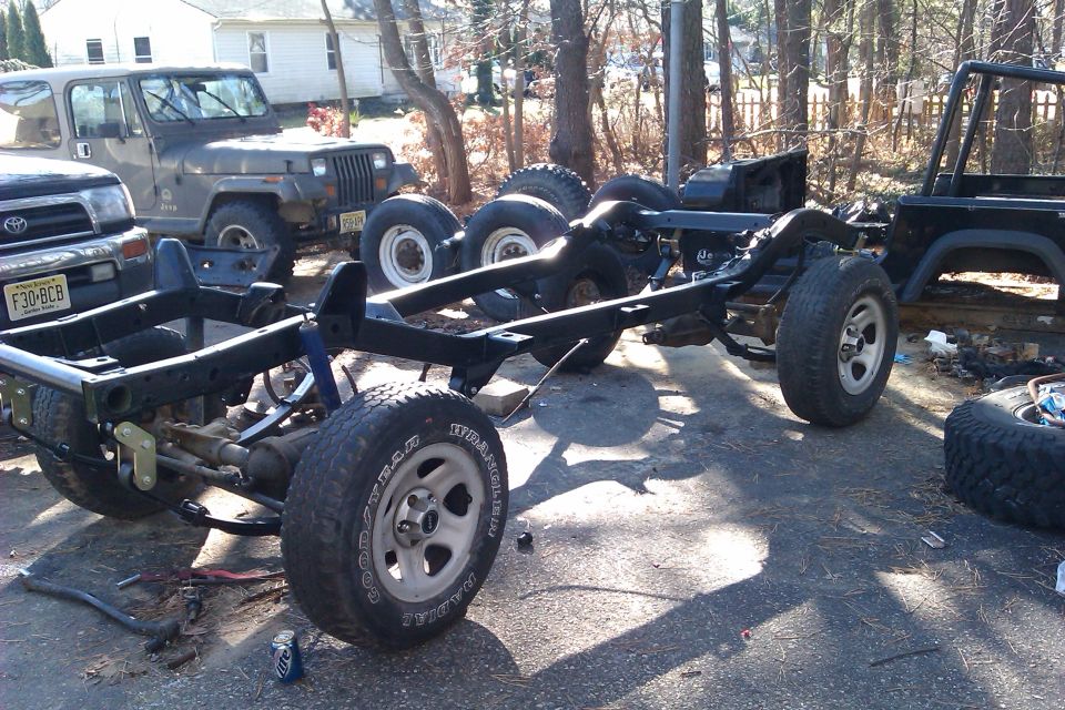 Jeep Wrangler frame with suspension and wheels, another Jeep Wrangler and a Toyota truck in background