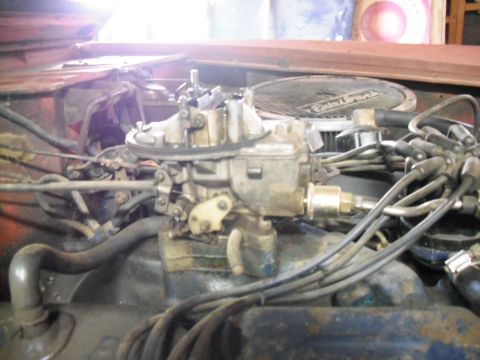 1968 Ford Bronco - Close-up down onto a four-barrel carburetor sitting on an intake manifold with the air cleaner removed, showing the throttle linkage, fuel…