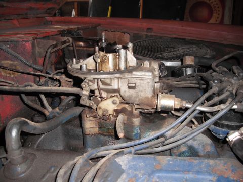 1968 Ford Bronco - Engine-bay close-up of a two-barrel carburetor on an intake manifold with the air cleaner off, showing the choke housing, brass fuel-inlet…