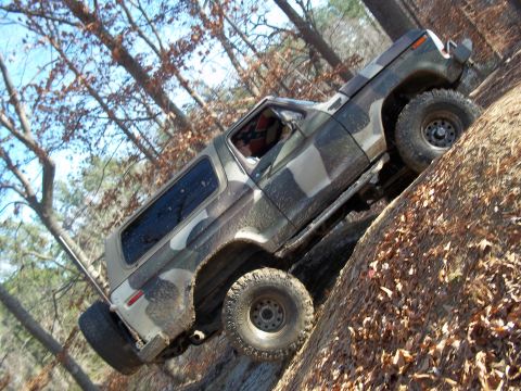 1979 Ford Bronco - This camouflaged SUV is navigating a challenging off-road trail with steep inclines and loose terrain.