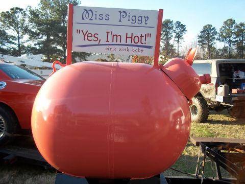 1979 Ford Bronco - A large, round, red pig sculpture is the main focus, with vehicles visible behind it.
