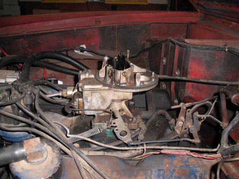 1968 Ford Bronco - Overhead engine-bay shot of a grimy two-barrel carburetor with the air cleaner removed, mounted on an intake manifold with the throttle lin…