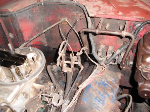 1968 Ford Bronco - Detail of a well-used engine bay showing the throttle and choke cables running from an uncovered carburetor at lower left across a blue-pai…