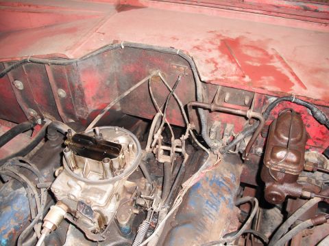 1968 Ford Bronco - Downward view into a dirty engine bay showing a two-barrel carburetor with its air cleaner removed and open throttle bores, a blue-painted…