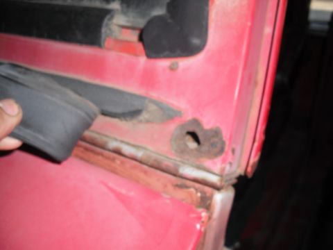 1968 Ford Bronco - Close-up of rust damage on a red vehicle's door frame, showing deterioration.