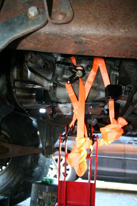 1982 Ford Bronco - Underneath view of a vehicle's transmission being supported by orange straps and a red jack.