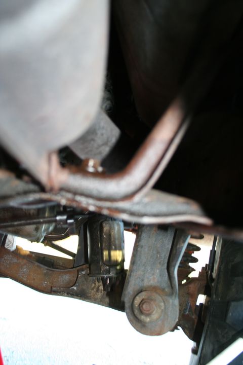1982 Ford Bronco - Close-up of the undercarriage, showing rusted metal parts and a small yellow fluid container.