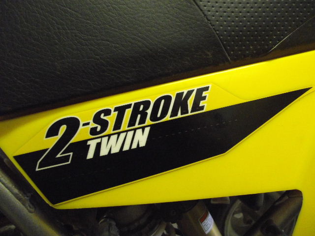 Close-up of a yellow motorcycle panel with a black decal that says "2-STROKE TWIN"