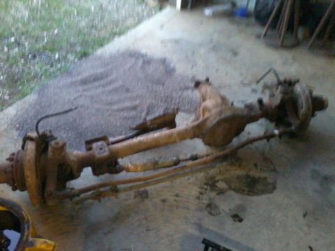 1995 Ford Bronco - A rusty rear axle assembly lies on a concrete surface, with grass and debris visible.