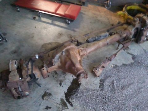 1995 Ford Bronco - Front axle assembly removed from a vehicle, lying on a garage floor.