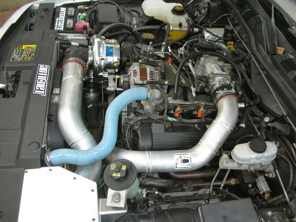 Engine bay with chrome supercharger, silver intake pipes, and blue hoses. "AUTOROT" sticker visible
