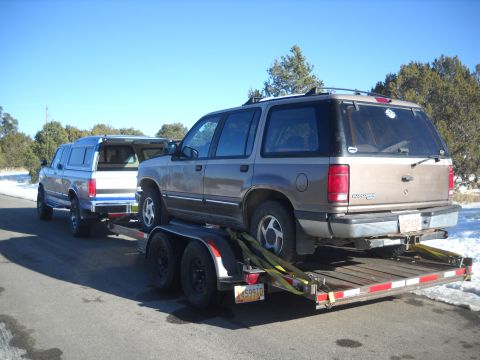 1992 Ford Explorer - A brown Ford Explorer is loaded onto a trailer, hitched to a blue Ford pickup truck under a clear sky.
