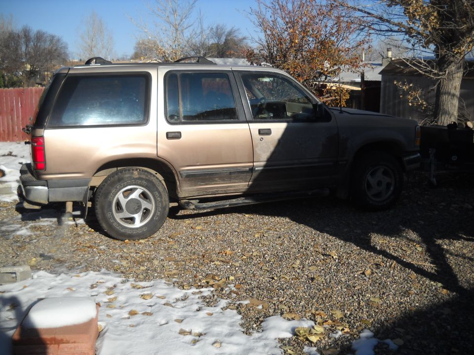 Tan and brown Ford Explorer SUV parked on gravel with snow patches