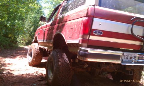 1987 Ford Bronco - A red 1987 Ford Bronco is seen off-road with its rear visible, showing lifted suspension and large tires.