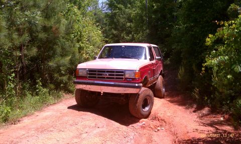 1987 Ford Bronco - Modified 1987 Ford Bronco navigating an off-road trail through a wooded area.