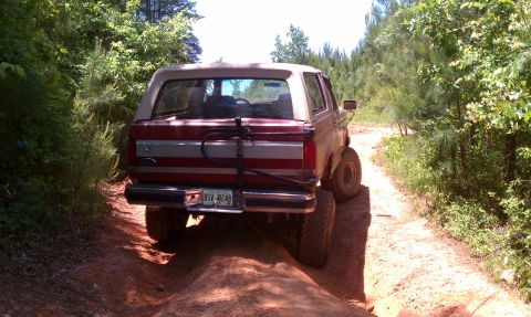 1987 Ford Bronco - A red 1987 Ford Bronco navigates a dirt path surrounded by trees.