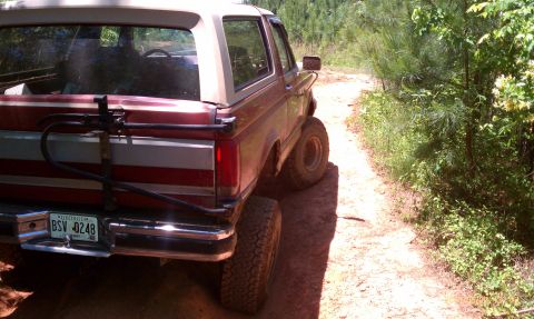 1987 Ford Bronco - This 1987 Ford Bronco is seen from the rear, driving on a dirt path surrounded by trees.