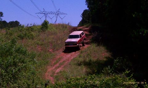 1987 Ford Bronco - This 1987 Ford Bronco navigates a dirt path under a clear blue sky, with power line towers visible in the background.
