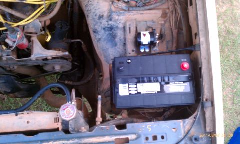 1987 Ford Bronco - The engine bay of a vehicle, a battery and wiring. The registry claims it is a 1987 Ford Bronco, but this is not verifiable from the image.