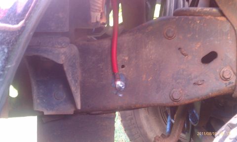 1987 Ford Bronco - Detail of a heavily rusted vehicle frame, showing a red wire connected to the chassis.