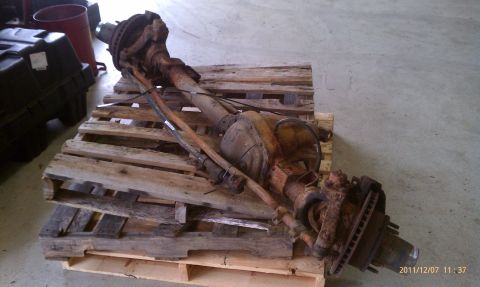 1987 Ford Bronco - A rusty front axle assembly, likely from a truck or SUV, rests on wooden pallets indoors.