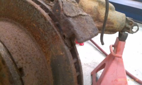 1987 Ford Bronco - Close-up of a heavily rusted brake rotor and part of a vehicle's suspension system.
