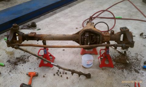 1987 Ford Bronco - A rusty front axle assembly, likely from an older truck or SUV, is supported by red jack stands on a concrete floor.