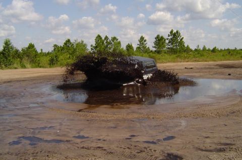 1995 Ford Bronco - A vehicle is submerged in a large mud pit, creating a significant splash.