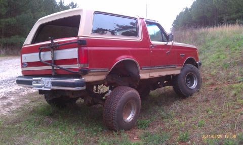 1987 Ford Bronco - This lifted 1987 Ford Bronco is shown from the rear three-quarter angle, its distinctive red and tan paint scheme and a rear-mounted spare…