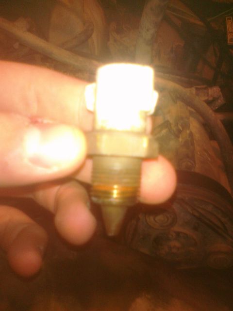 1995 Ford Bronco - A hand holds a small automotive sensor with a tan/white plastic housing, hex nut base, and threaded tip with an orange O-ring, likely a coo…
