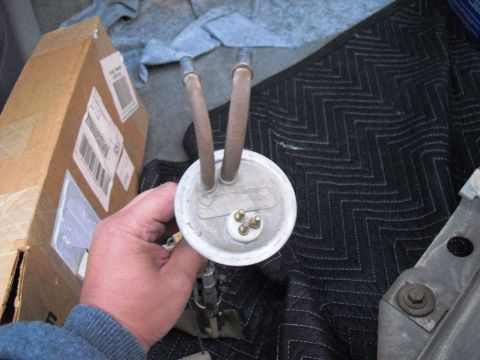 1986 Ford Bronco - A person holds a fuel pump assembly, likely for replacement, with a box and quilted padding in the background.