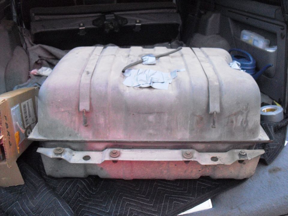 Fuel tank with straps and fuel line, resting on a quilted mat inside a vehicle cargo area
