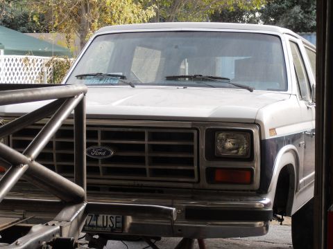 1986 Ford Bronco - The front end of a 1986 Ford Bronco is visible, the Ford emblem on the grille and a custom roll cage in the foreground.