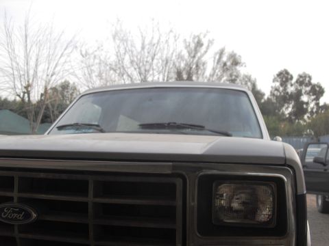 1986 Ford Bronco - Front view of a 1986 Ford Bronco, showing the grille and headlight assembly. Another vehicle is partially visible to the right.