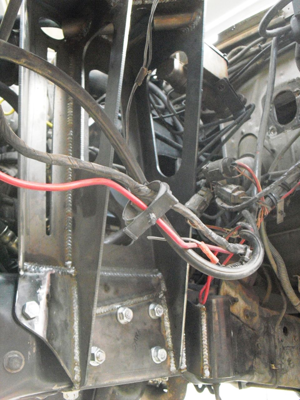 Custom metal brackets and red wiring are bolted to a vehicle's frame