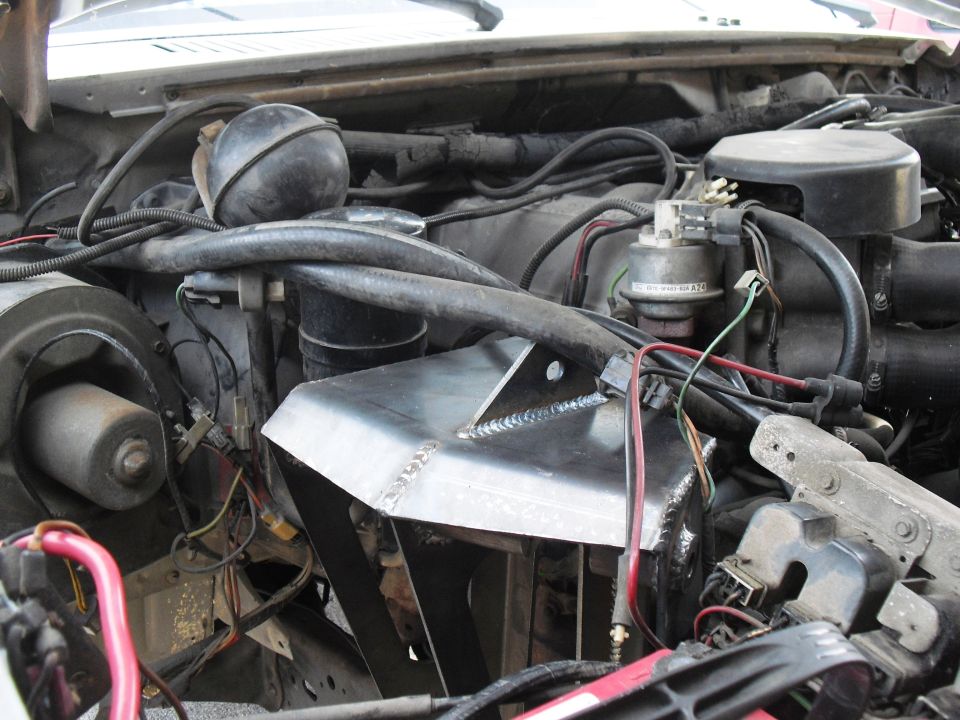 Engine bay showing wiring, hoses, and a custom-welded metal component over the engine block