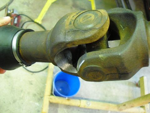 1986 Ford Bronco - A driveshaft universal joint is shown in detail, with a blue bucket in the background.