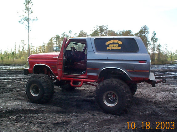 Lifted red and gray Ford Bronco with open driver door, sitting in mud