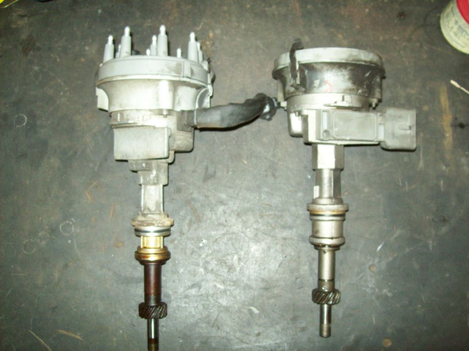 Two Ford V8 distributors side by side on concrete, one with cap on, one with cap removed