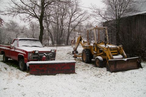 2000 Chevrolet Tahoe - Two vehicles, a pickup truck and a backhoe, sit in a snowy yard with a barn in the background.