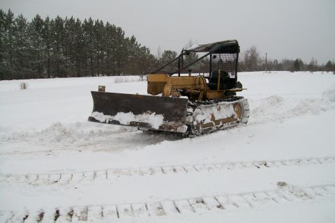 2000 Chevrolet Tahoe - A yellow crawler tractor equipped with a front plow operates in a snow-covered field.