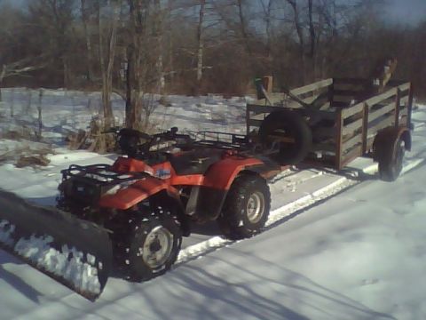 2000 Chevrolet Tahoe - An ATV equipped with a snow plow attachment tows a wooden trailer through a snowy landscape.