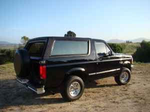 1996 Ford Bronco - This black SUV is parked outdoors on a dirt lot with a spare tire on the rear.