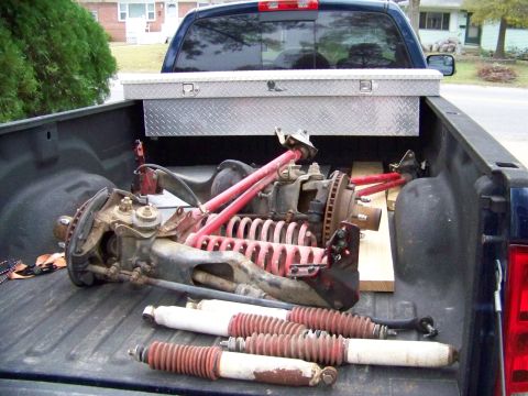 1985 Ford Bronco - Various suspension parts are loaded into the bed of a pickup truck, along with a metal toolbox.