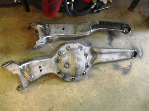 1986 Ford Bronco - Two custom metal automotive parts, possibly a rear axle housing and a control arm, are shown on a workshop floor.