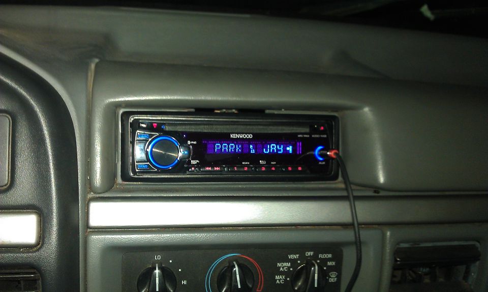Kenwood head unit in gray truck dash showing PARK JAY, with aux cable plugged in