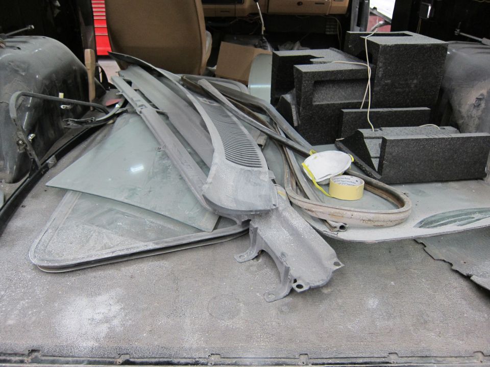 Dust-covered car parts including glass, trim, and a windshield wiper cowl