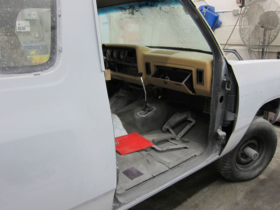 Interior of a 1987 Dodge 1500 pickup truck, showing the dashboard, floor, and open door